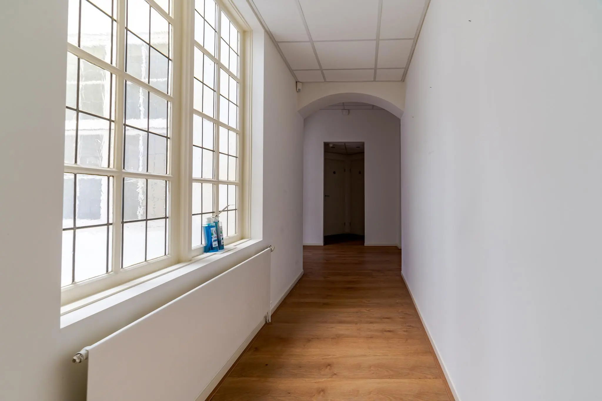 Lichte gang met houten vloer, grote ramen aan de linkerkant en een nis aan het einde in een gebouw aan het Lange Voorhout.